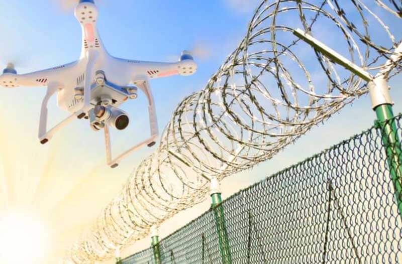 White drone equipped with a camera hovering over a barbed wire fence