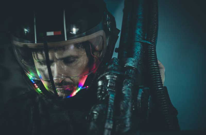 Man holding a weapon and wearing a futuristic helmet with some kind of liquid in it