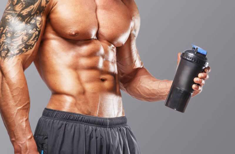 A muscular man without a shirt holding a black sports bottle