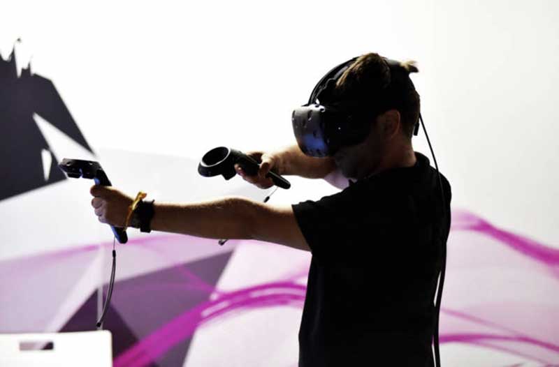 A person in a black t-shirt wearing a VR headset and holding VR controllers