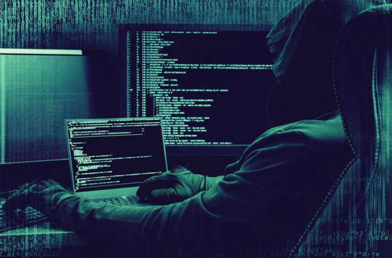 Een hacker met een hoodie zit in een donkere ruimte en kijkt naar een computerscherm met computercode