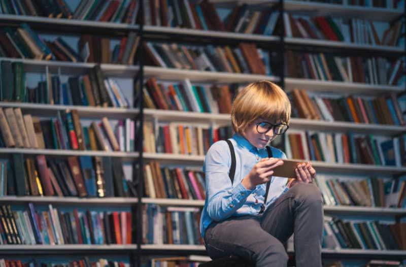 A child sitting in a library looking at a smartphone