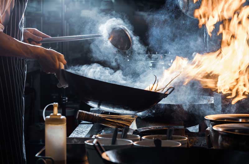 Person preparing food in a frying pan on high heat, causing burning and smoke