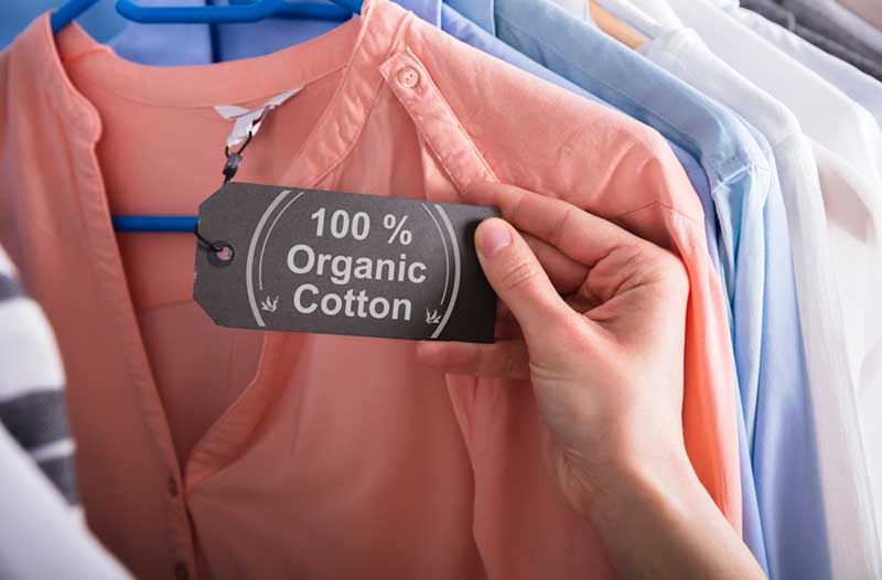A hand holding a “100% organic cotton” certification label on a peach-coloured shirt
