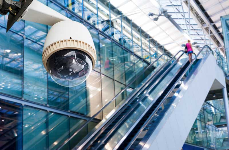 A video surveillance camera in a shopping mall with escalators and large glass walls