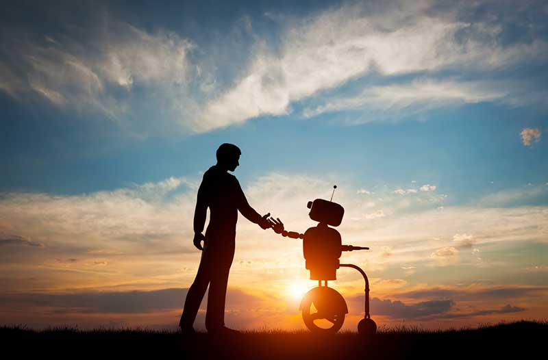 Silhouettes of a man and a robot touching hands with the Sun in the background