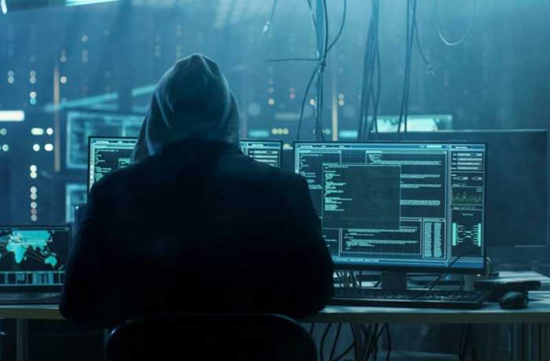 Achteraanzicht van een man met een hoodie die voor computerschermen zit