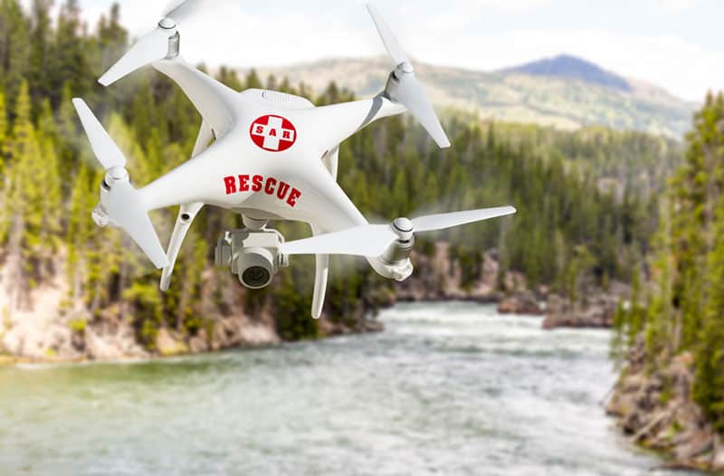 A white drone with the word rescue on it flying over a river, with mountainous landscape in the background